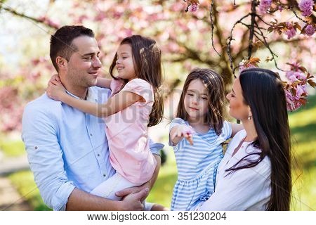 Young Parents With Small Daugthers Standing Outside In Spring Nature.