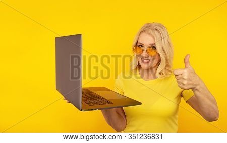 Portrait Of Happy Exited Abult Lady With Laptop Isolated Over The Yellow Studio.
