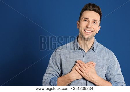 Handsome Grateful Man With Hands On Chest Against Blue Background