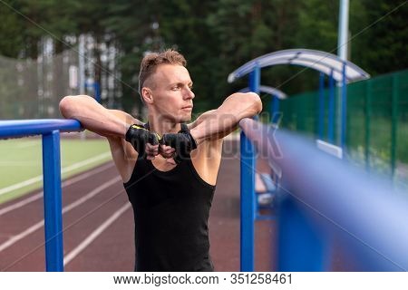 A Muscular Man Stands Leaning On Parallel Bars, With A Bare Torso.