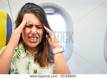 Young traveller woman sitting inside plane at the airport with sky view from the window feeling sick, headache and nauseas