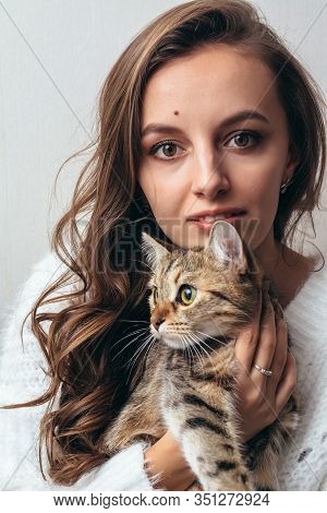 Girl In A White Sweater Hugs A Gray Cat On A White Background.