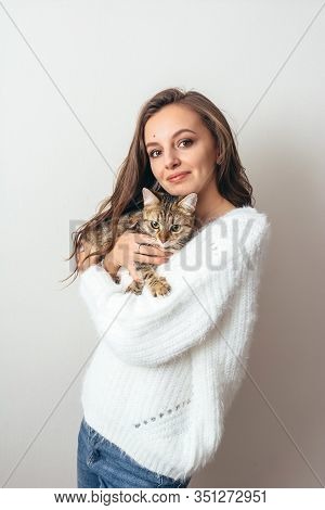Girl In A White Sweater Hugs A Gray Cat On A White Background.