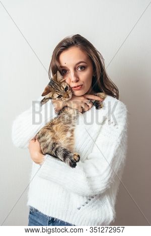 Girl In A White Sweater Hugs A Gray Cat On A White Background.