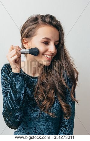 Beautiful Young Woman In Shiny Green Dress Applying Powder With A Brush To The Face.