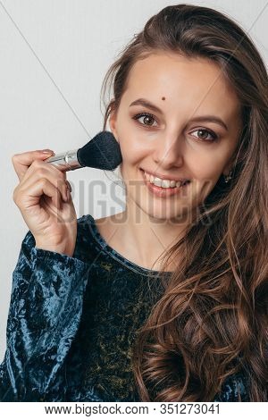 Beautiful Young Woman In Shiny Green Dress Applying Powder With A Brush To The Face.