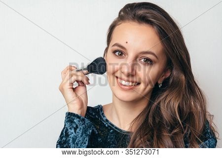 Beautiful Young Woman In Shiny Green Dress Applying Powder With A Brush To The Face.