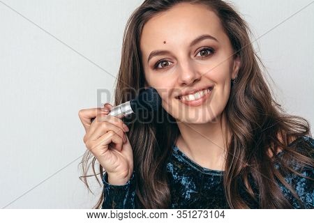 Beautiful Young Woman In Shiny Green Dress Applying Powder With A Brush To The Face.