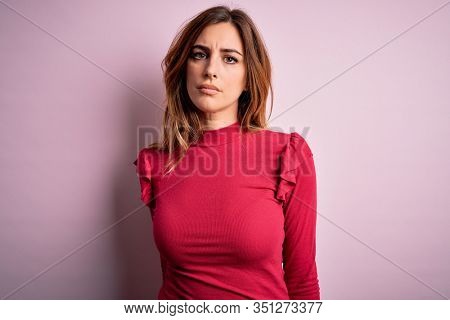 Young beautiful brunette woman wearing casual sweater stnding over pink background with serious expression on face. Simple and natural looking at the camera.