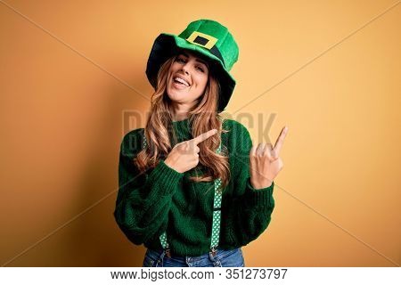 Beautiful brunette woman wearing green hat with clover celebrating saint patricks day smiling and looking at the camera pointing with two hands and fingers to the side.
