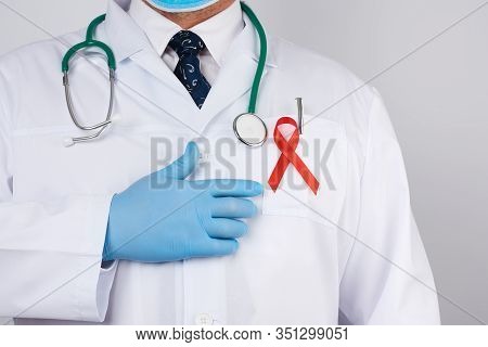 Male Doctor In A White Coat And Tie Is Standing On A White Background, Red Silk Ribbon Is Hanging On