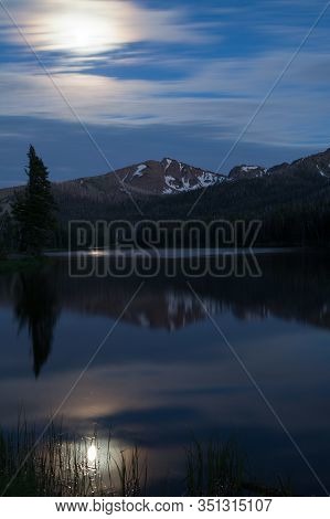 The Full Moon Over Top Notch Peak Is Reflecting Light Onto Sylvian Lake In Yellowstone National Park