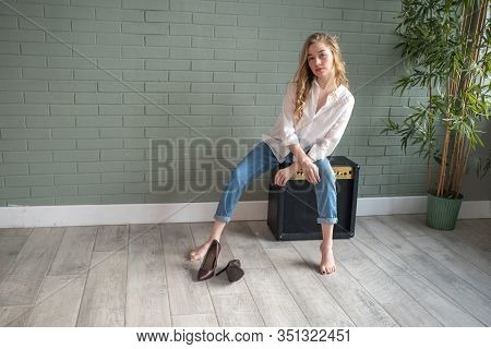 Young Beautiful Woman Sitting On Subwoofer With Bare Feet Next To Green Plant