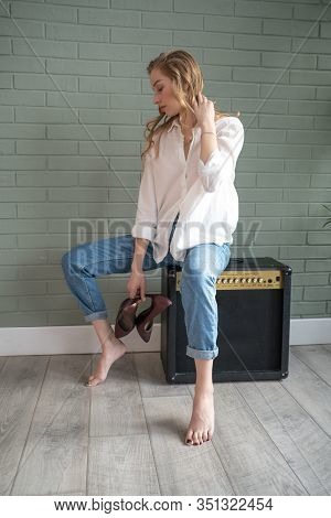 Young Beautiful Woman Sitting On Subwoofer With Bare Feet Next To Green Plant