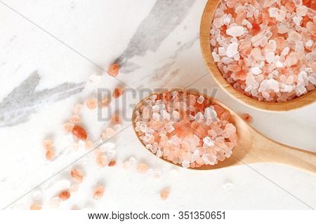 Top View Of Himalayan Pink Rock Salt In Wooden Bowl And Spoon On White Marble Table.