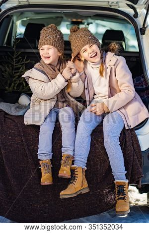 Two Sisters Sitting At The Top In The Trunk Of A Car And  Pull The Tail. Outdoors In The Winter.