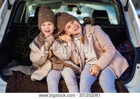 Two Sisters Sitting At The Top In The Trunk Of A Car And  Pull The Tail. Outdoors In The Winter.