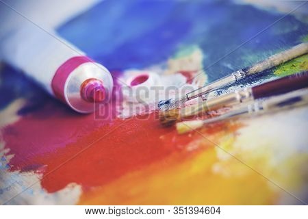 An Open Tube Of Pink Oil Paint And Three Paint Brushes Lie On A Bright Palette That Is Stained With 