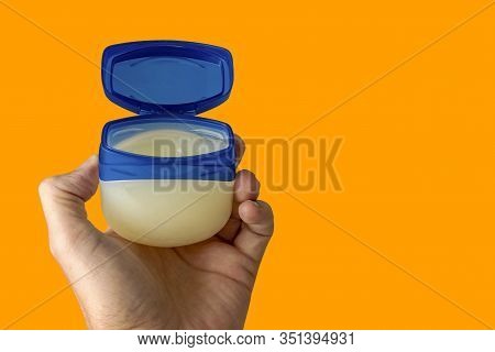 The Left Hand Of A Male Person Holds A Container With Vaseline Or Cream. The Background Is Out Of Fo