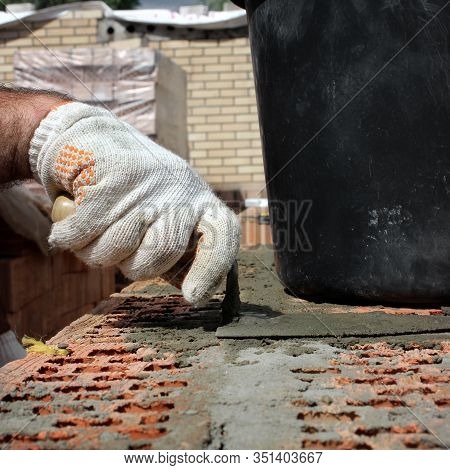 Bricklayers Hands With In Masonry Trowel Bricklaying New House Wall On Foundation. Close Up Of Indus