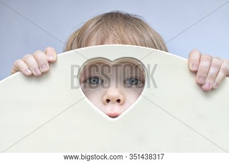 Baby Boy Toddler Face, Eyes And Nose Peep Out Of Heart-shaped Hole In Center. A Child Looks Into Cam