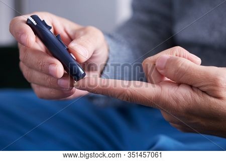 closeup of a caucasian man about to measure his blood glucose level in a glucose meter by pricking his finger with a fingerstick