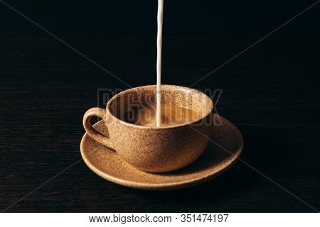 Milk Is Pouring Into A Cup Of Coffee On A Black Background.