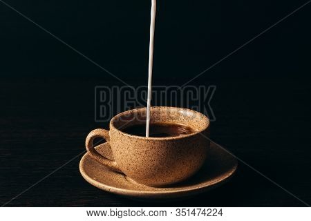 Milk Is Pouring Into A Cup Of Coffee On A Black Background.