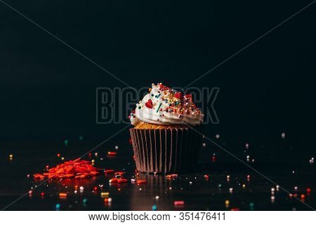 Cupcake Sprinkled With Decorations On A Black Background.