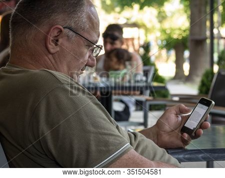 Alibunar, Serbia - June 6, 2015: Oldd Sernior White Man Sitting In A Cafe Looking At An Apple Iphone