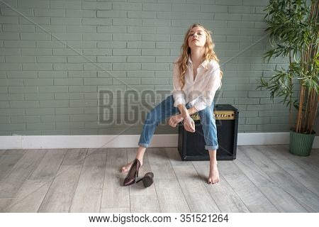 Young Beautiful Woman Sitting On Subwoofer With Bare Feet Next To Green Plant