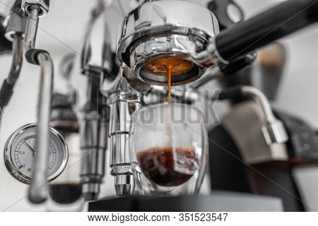 Coffee machine pouring single shot espresso in double wall glass from bottomless naked portafilter. Professional equipment at home or cafe.
