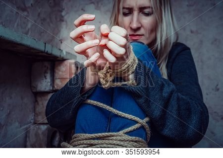 Blonde Girl With Her Hands And Feet Tied Is Sitting In The Basement. Concept Of Kidnapping, Violence