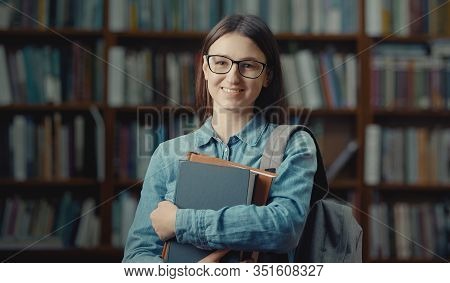Portrait Of Lovely Smiling Female Student With Glasses And Backpack Holding Books Looking Camera