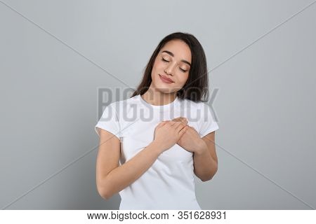 Beautiful Grateful Woman With Hands On Chest Against Light Grey Background