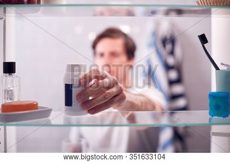 View Through Bathroom Cabinet Of Man Taking Medication From Container