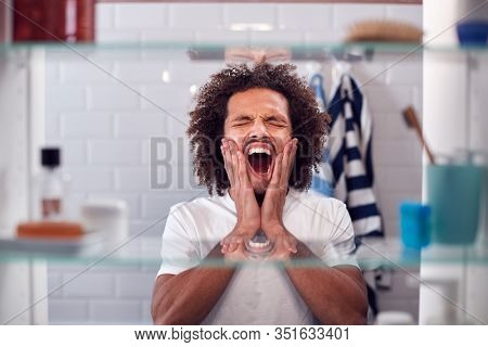 View Through Bathroom Cabinet Of Yawning Man Getting Ready For Work In The Morning
