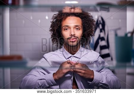 View Through Bathroom Cabinet Of Young Businessman Putting On Shirt Getting Ready For Work