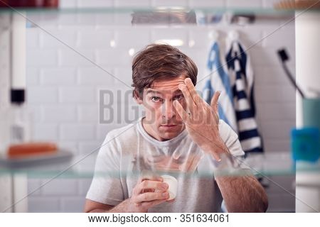 View Through Bathroom Cabinet Of Man Getting Ready For Work And Moisturizing Skin