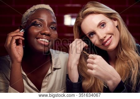 Two Young Female Friends Doing Make Up Reflected In Mirror Of Bathroom In Club