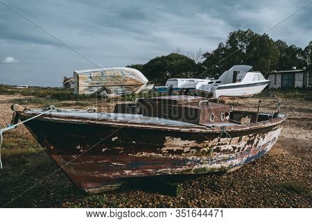 An Abandoned Wooden Fishing Boat With A Small Cabin And Flacked Timbers On A Pebble Ground Of A Shal