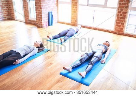 Young beautiful group of sportswomen smiling happy practicing yoga. Lying down doing corpse pose at gym