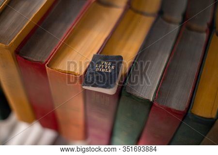 The Small Holy Book Of The Bible Lies On Large Multi-colored Books.