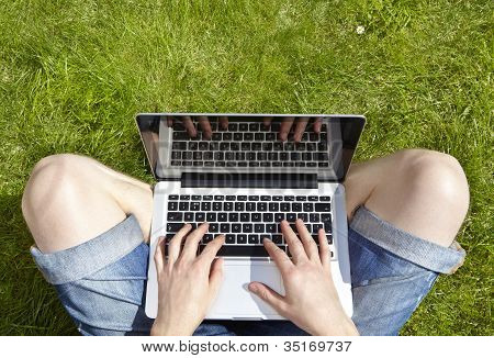 Człowiek za pomocą laptopa siedząc na trawie