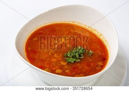Beef Goulash Soup With Tongue. A White Oval Plate With Red Soup Stands On A White Background.