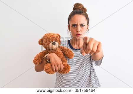 Young beautiful redhead woman holding stuffed teddy bear over isolated background pointing with finger to the camera and to you, hand sign, positive and confident gesture from the front