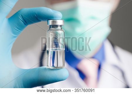 Close Up Hand Of Doctor In Blue Latex Glove And Medical Gauze Mask With Glass Ampoule. Health And Va