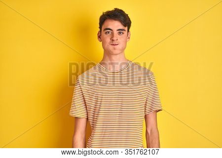 Teenager boy wearing yellow t-shirt over isolated background puffing cheeks with funny face. Mouth inflated with air, crazy expression.