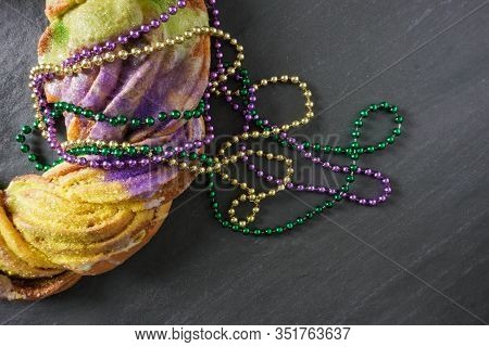 Festive Gold, Green And Purple Beads Draped Over A Mardi Gras King Cake On A Gray Slate Background W