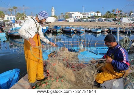 Mahdia, Tunisia - December 27, 2019: Fishermen Repairing Their Net At The Fishing Port, With The Cit